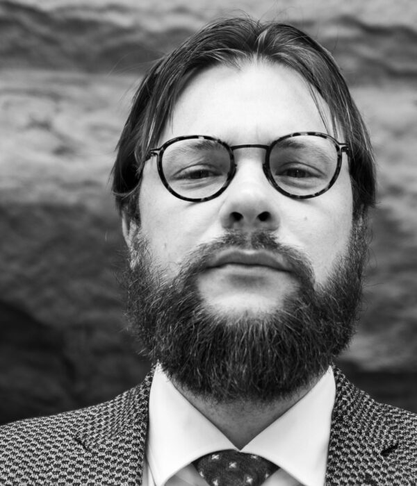 A man with beard and glasses in front of a rock wall.