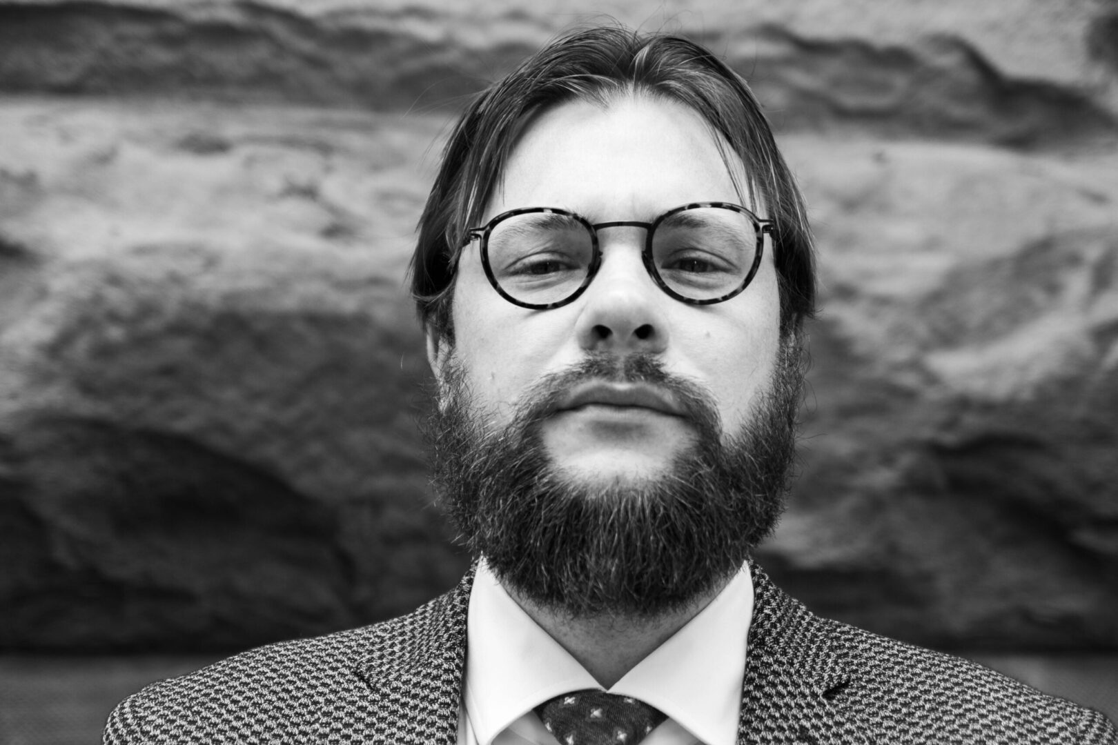 A man with beard and glasses in front of a rock wall.