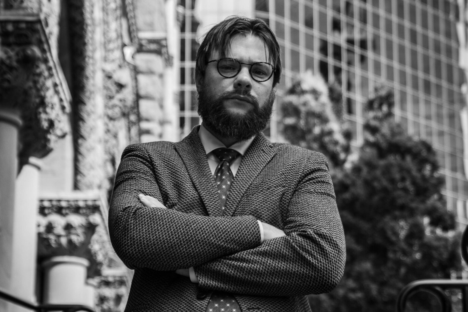 A man with beard and glasses standing in front of a building.