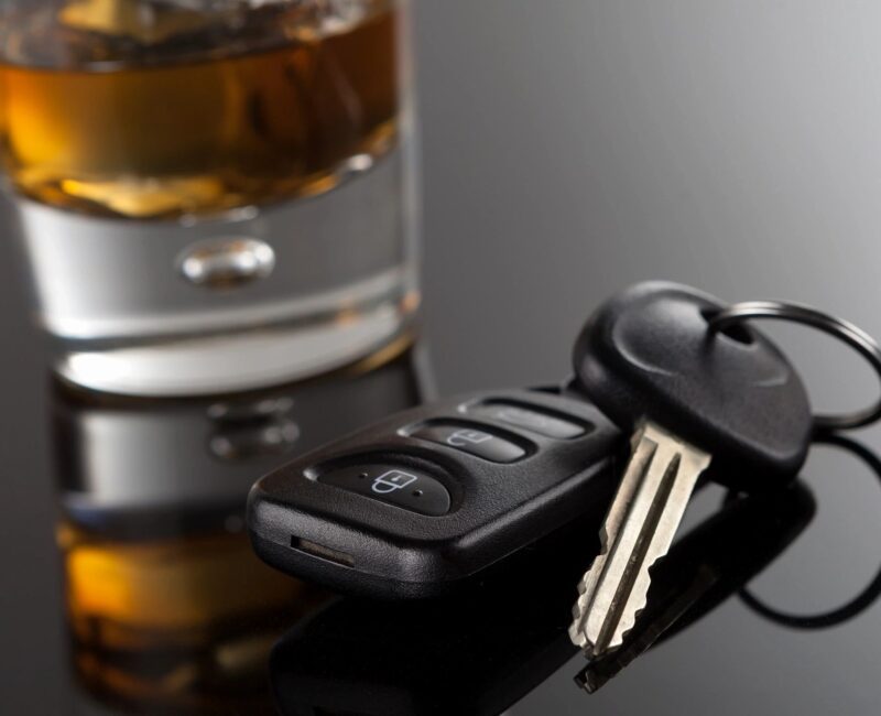 A car key sitting next to a glass of alcohol.