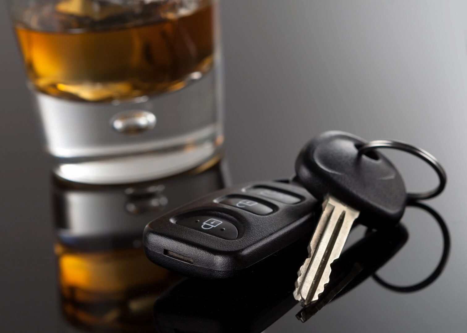 A car key sitting next to a glass of alcohol.