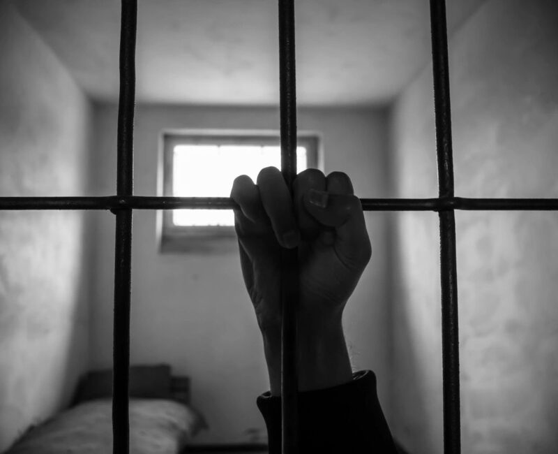 A person 's hand is holding onto bars in a jail cell.